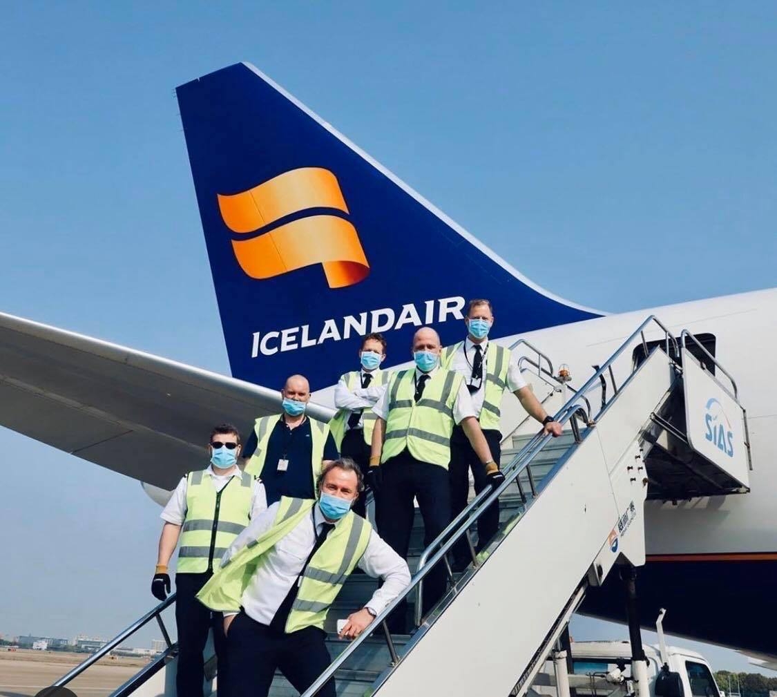 A group of Icelandair staff wearing masks as they stand on the aircraft stairs, with a view of the Icelandair aircraft behind them