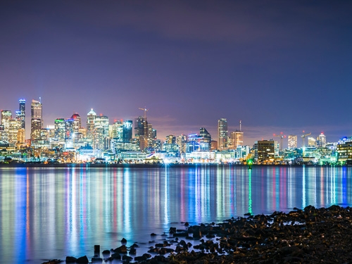 The skyline of Seattle pictured in the evening light with city lights reflected on the water 