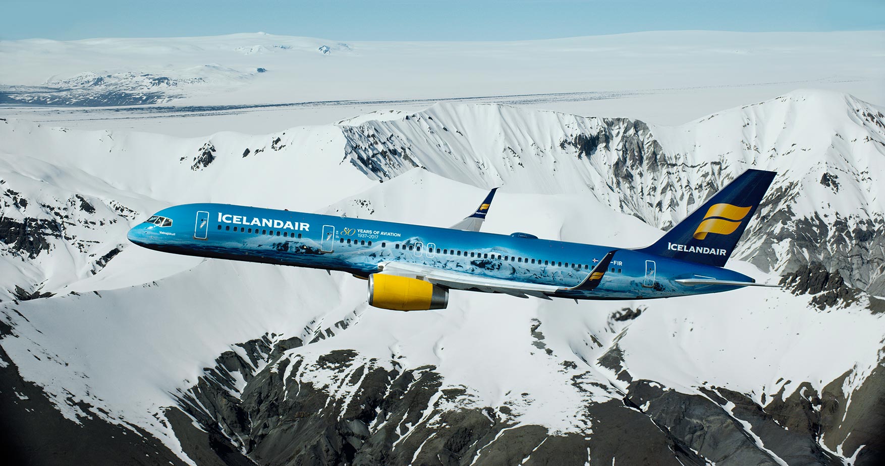 An Icelandair plane with a spraypaint design to pay tribute to Vatnajokull glacier, flying over snowy mountains in ICeland