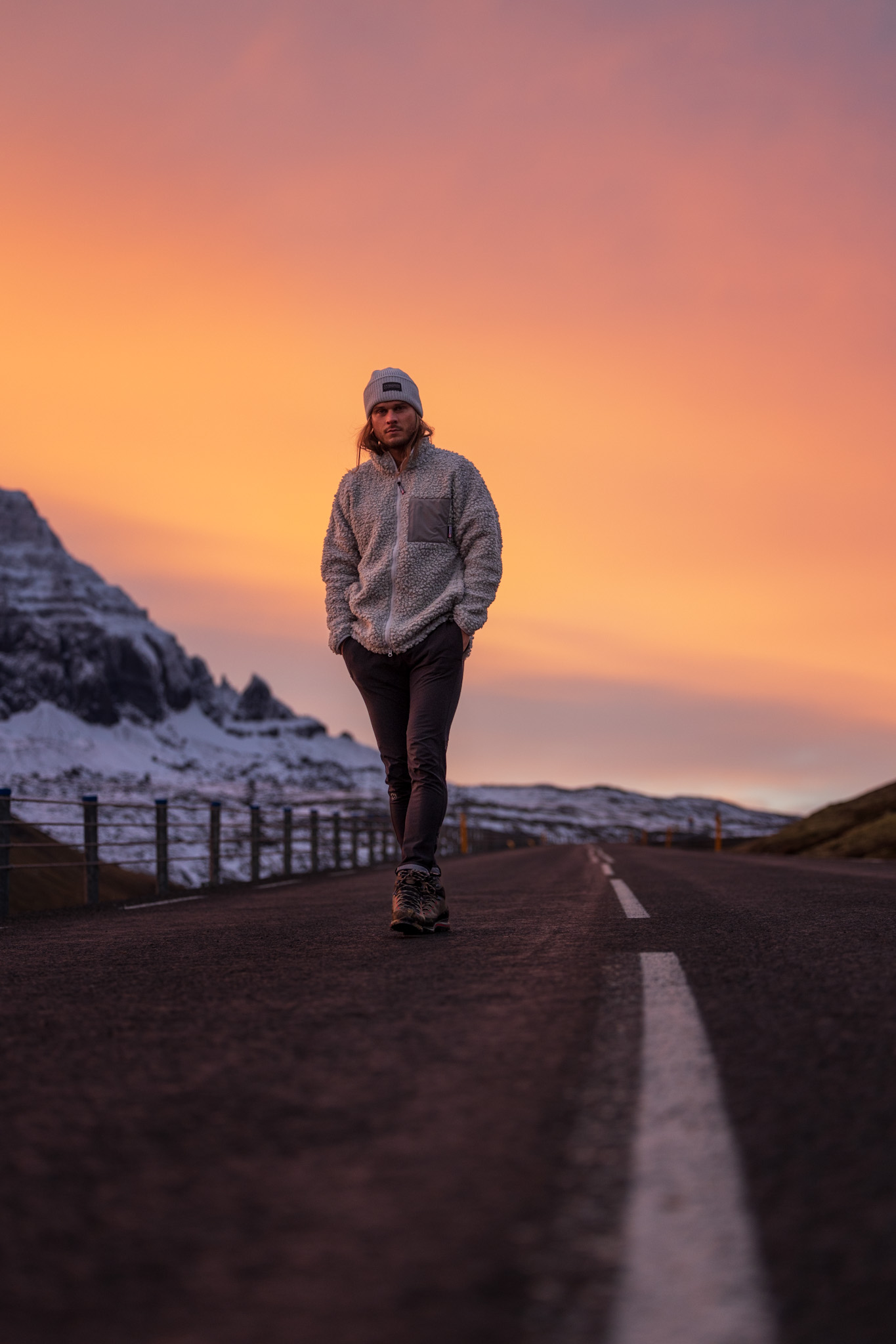 Rúrik Gíslason stands on a road with an orange-sky sunset behind him, and a backdrop of snowy peaks