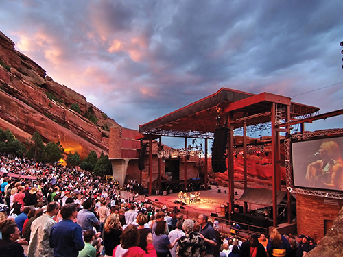 A performer takes to the stage at the Red Rocks amphitheater in Denver, with a large crowd watching 