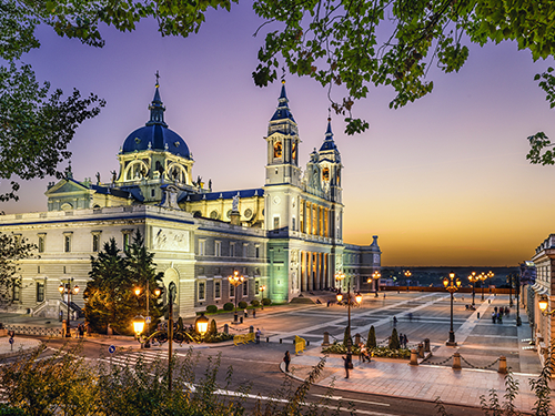 Catedral de la Almudena in Madrid lit up in gentle dawn light, with the sky a combination of purples, oranges and yellows 
