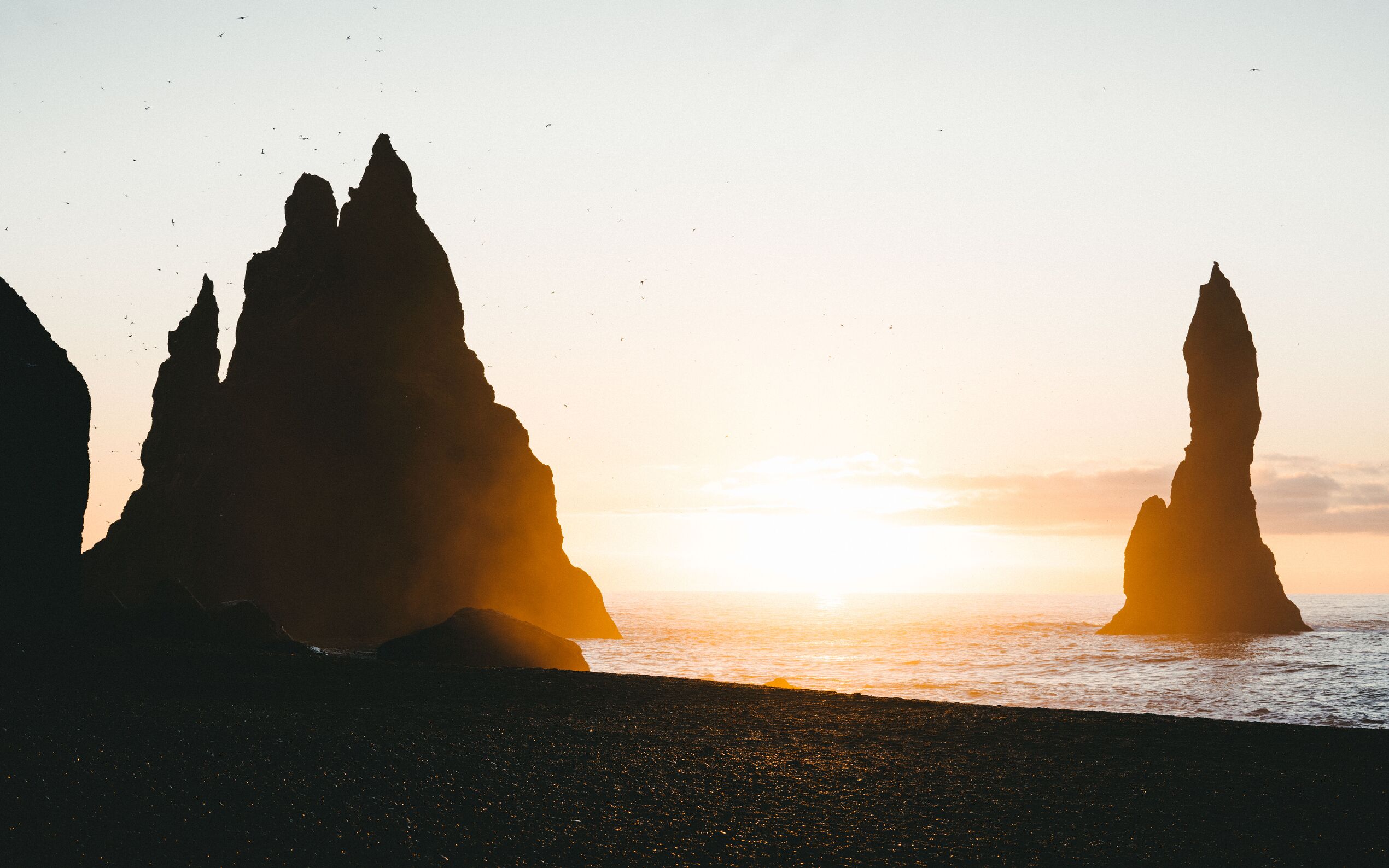 View of the sea stacks at Reynisfjara with the sun sitting low on the horizon and birds circling overhead