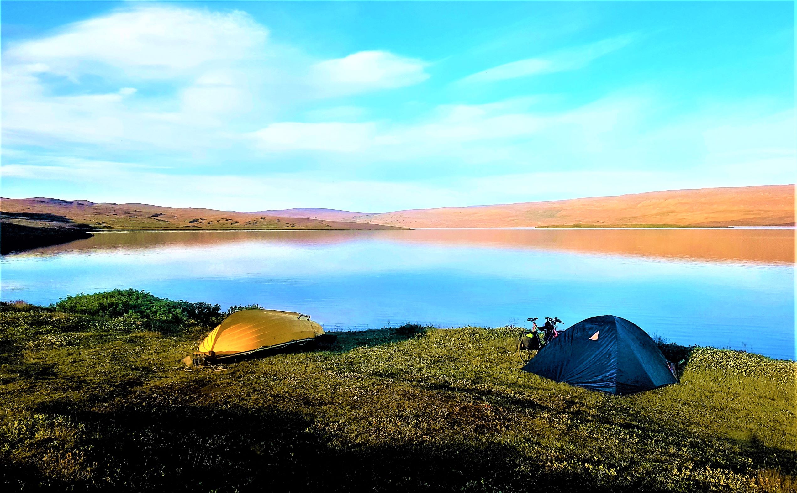 Two tents - one yellow, one blue - pitched next to a lake in Iceland on a bright and sunny day