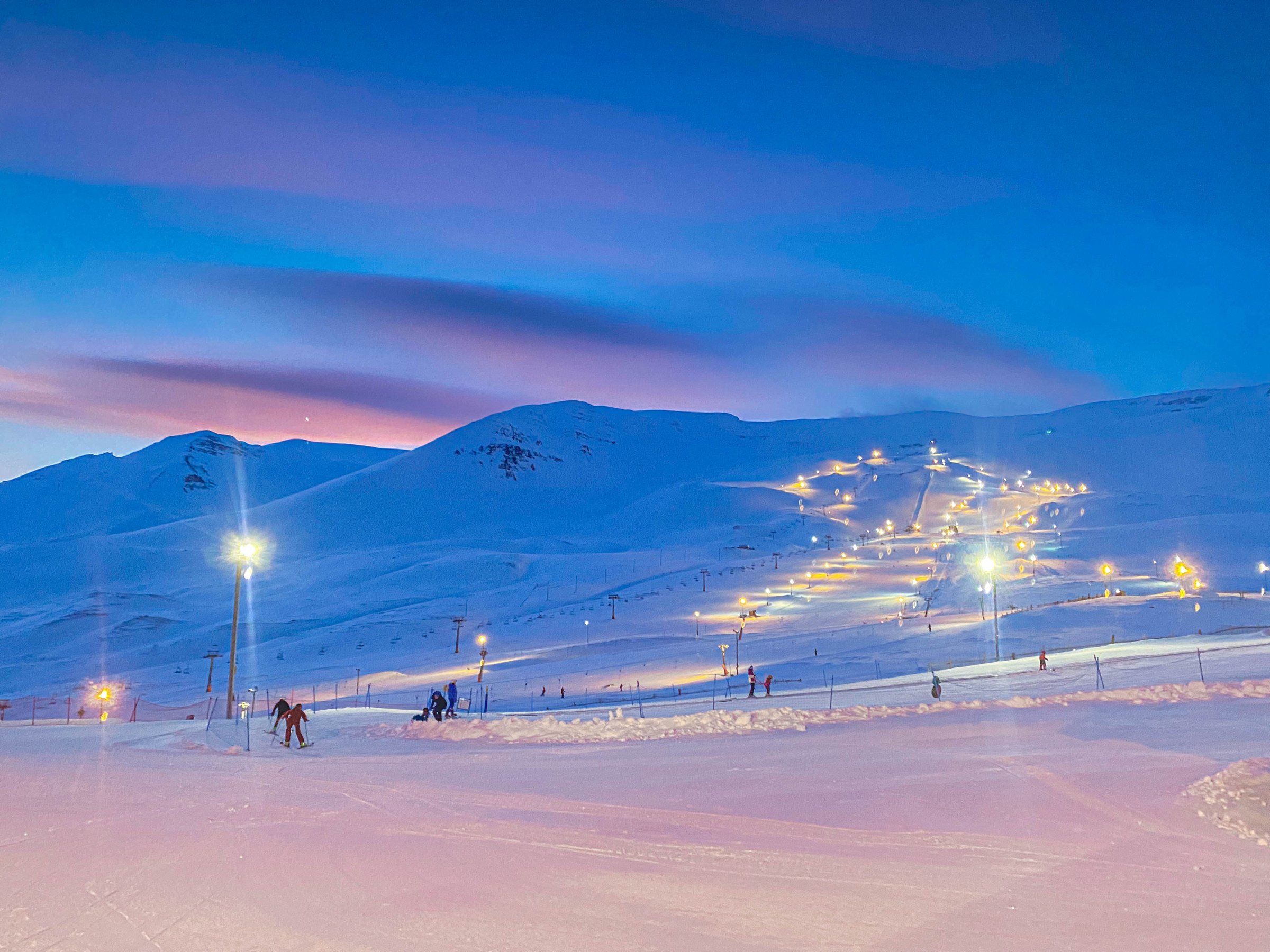 Twilight view of skiers and floodlit ski runs covered in snow