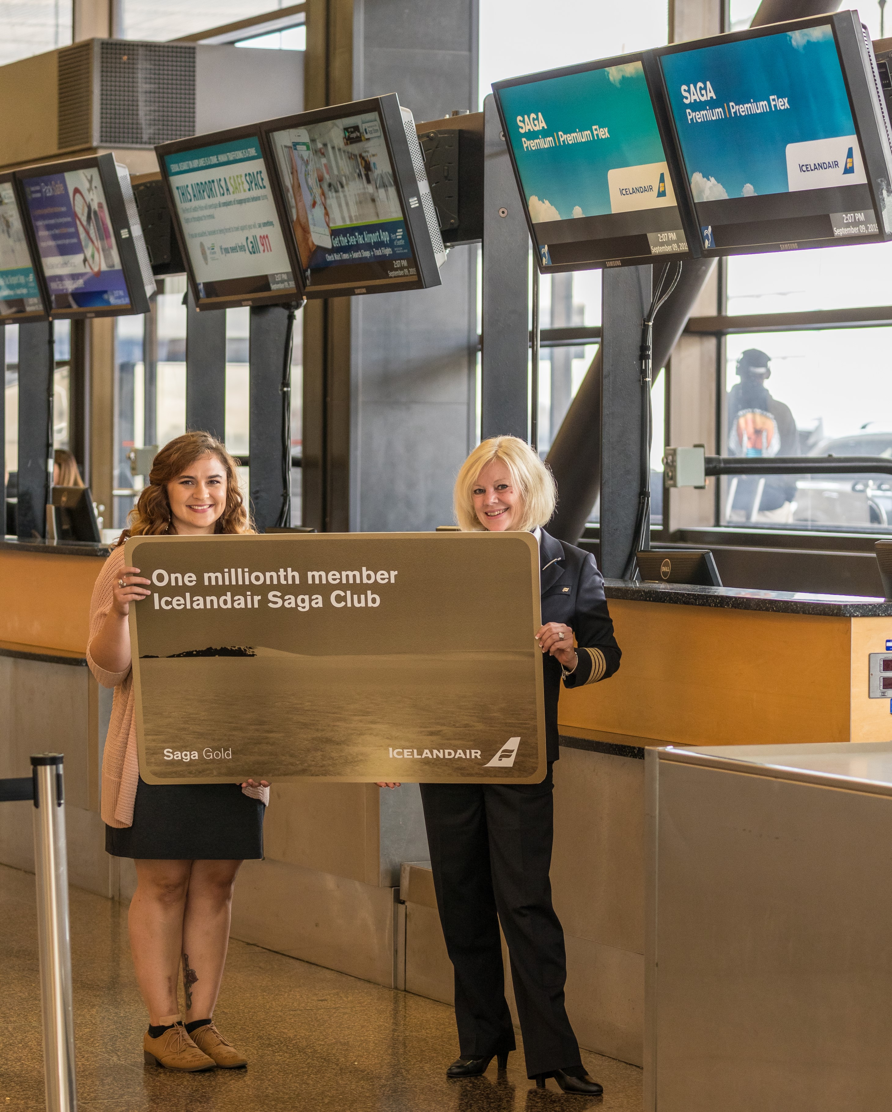 Hayley Nichols and Jessica Ginger pictured in the airport holding a large gold Icelandair Saga Club card with text that reads 'One millionth member'