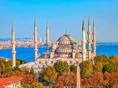 The Blue Mosque in Sultanahmet, Istanbul on a sunny day, surrounded by greenery and with a deepblue sea in the background