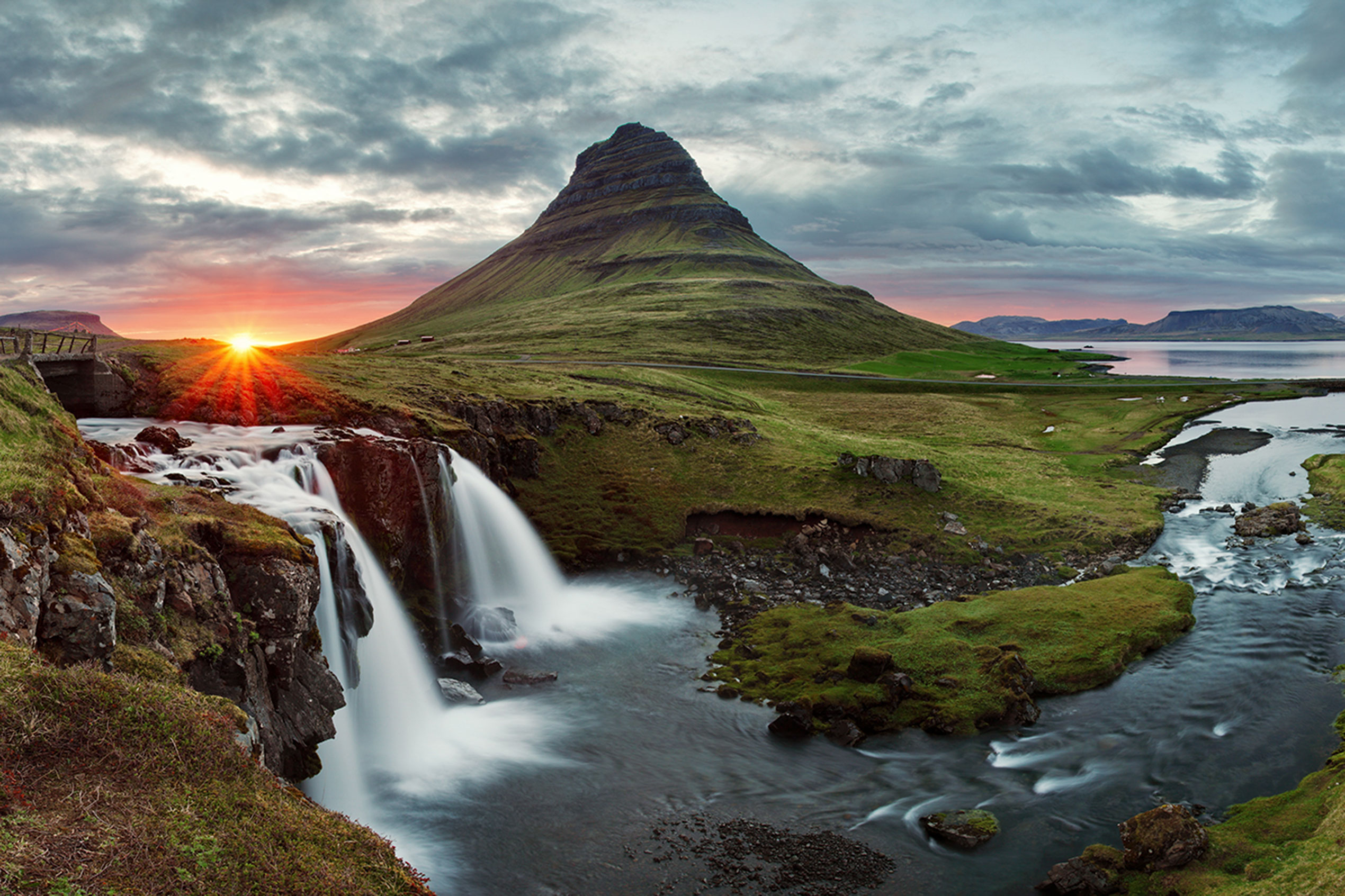 Kirkjufell and kirjufellsfoss waterfall pictured during the midnight sun with the sun setting just behind the mountain