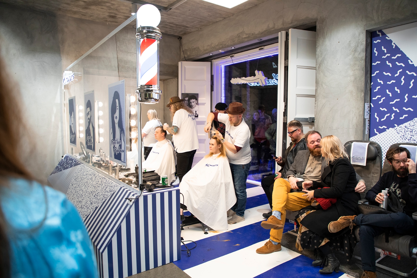 Hairdressers wearing white t-shirts that read 'Hairwaves' cut the hair of people sitting facing mirrors in the hair salon at Iceland Airwaves