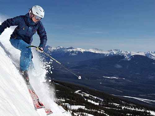 A person wearing light blue trousers and a dark blue jacket skis down the snowy slopes in Canada 