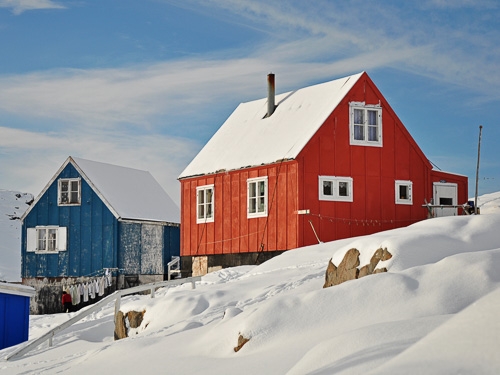 Two houses (one red, one blue) pictured against a snowy scene in Kulusuk, Greenland 