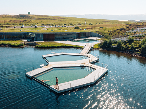 Et luftfoto af Vök-badene i det østlige Island på en lys dag med to personer, der nyder faciliteterne 