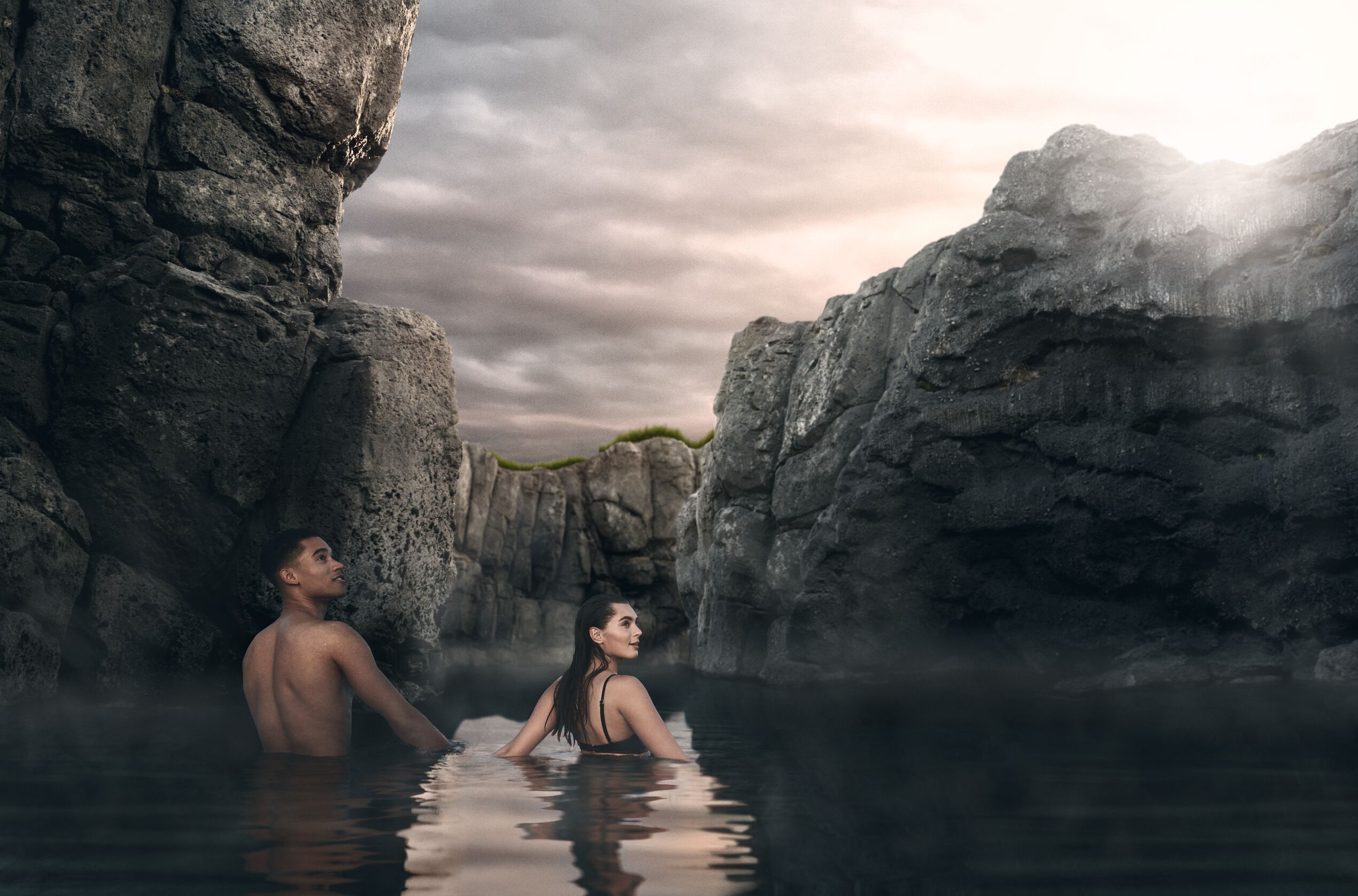a man and a woman looking to the side, while standing in a steep gully in the Sky Lagoon baths.