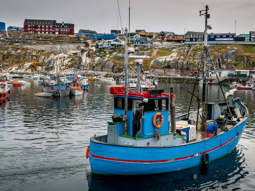 A man stands on a blue and red boat which is pictured in the bay at Ilulissat, Greenland 