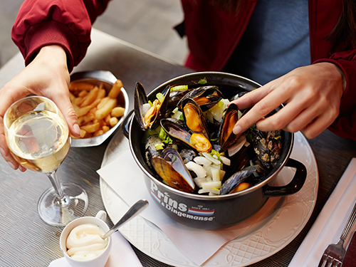 A large dish of mussels is here pictured with chips as a side dish and a glass of white wine on the table  
