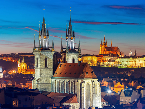 A view of one of the Spires in Prague, set against the night sky and city lights behind it
