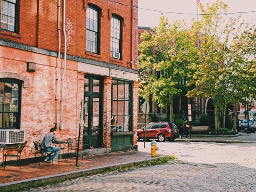 A street view of a red brick cafe where someone sits outside drinking coffee 