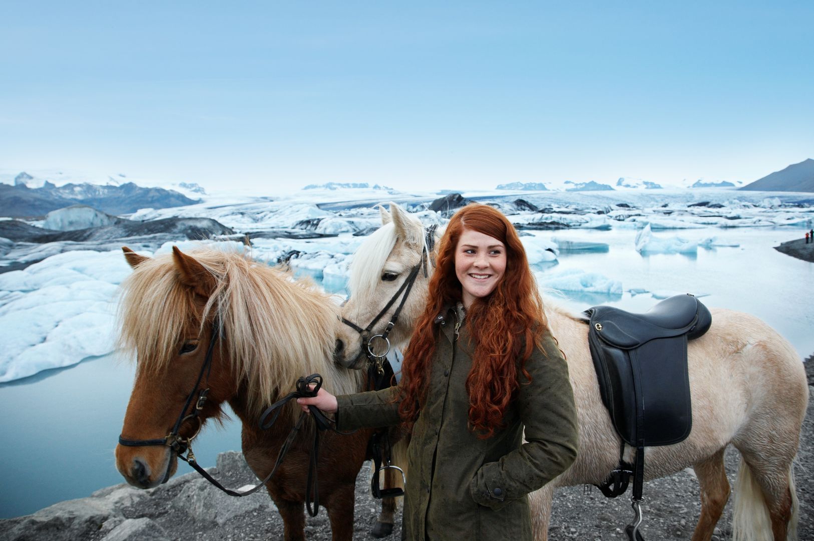 a white redhaired female smiling while standing next to two horses at Jokulsarlon glacier lagoon