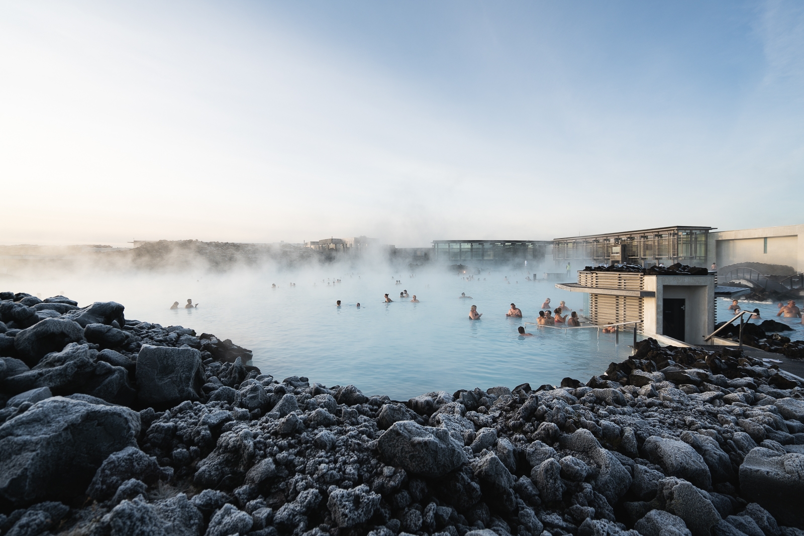 Swimmers in the steaming water at the Blue Lagoon complex, with black lava in the foreground