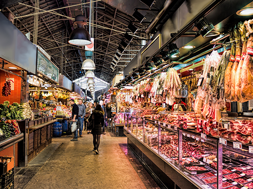 A busy market in Barcelona, with meat hanging to the right of the picture at the butcher’s stand 