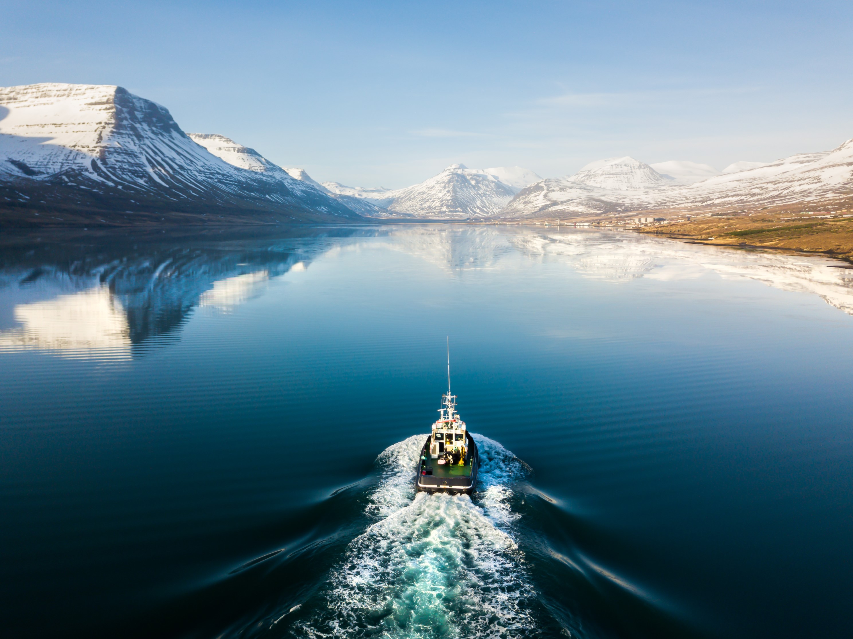 a boat sailing down a fjord in Iceland, surrounded by mountains and crystal blue sky