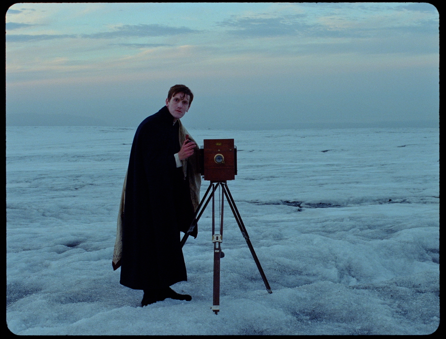 Production photo from the set of Godland the movie, showing the Danish priest posing with his camera, taking a photo