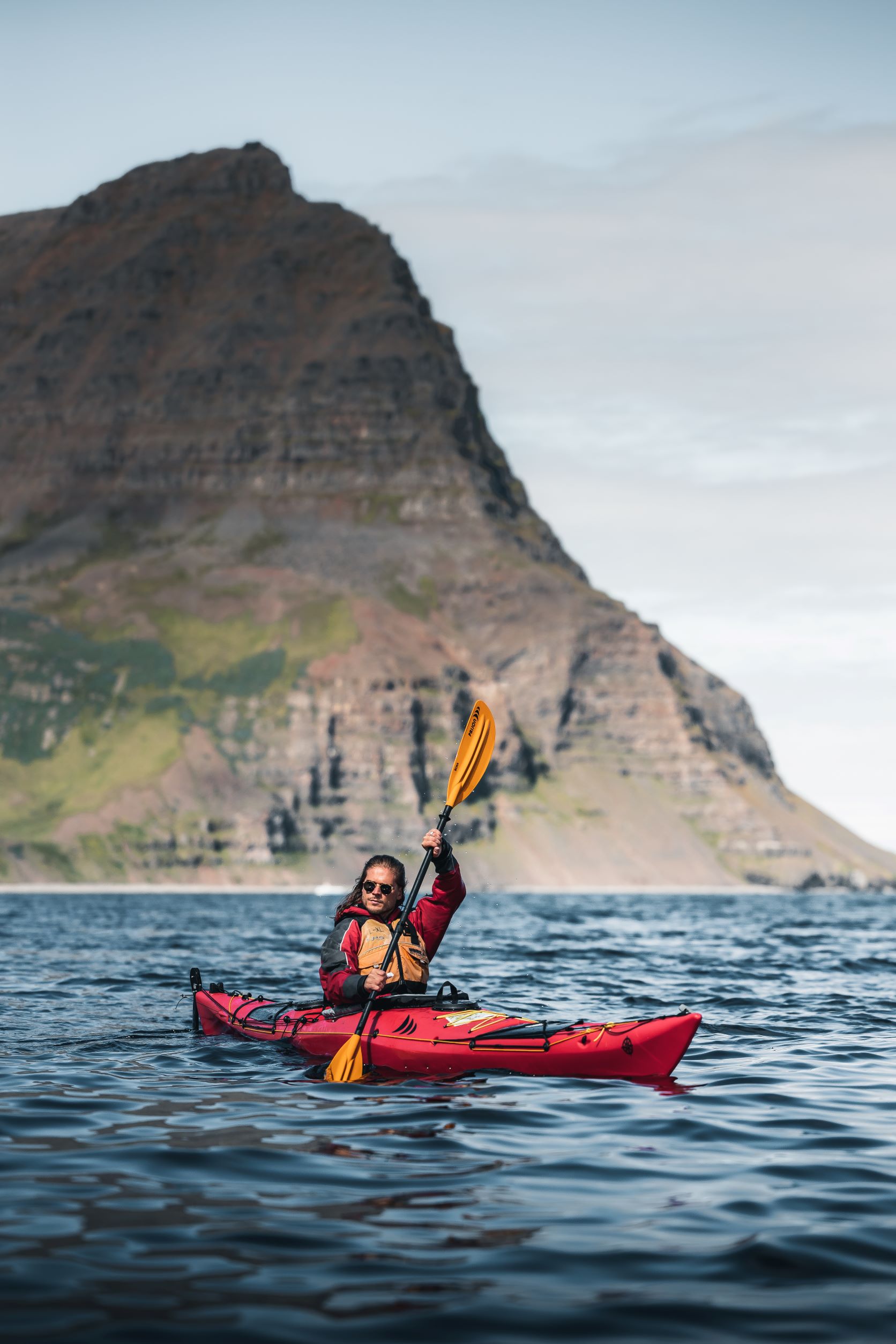 Rurik Gislason in a kayak on a fjord, with a mountain rising in the background