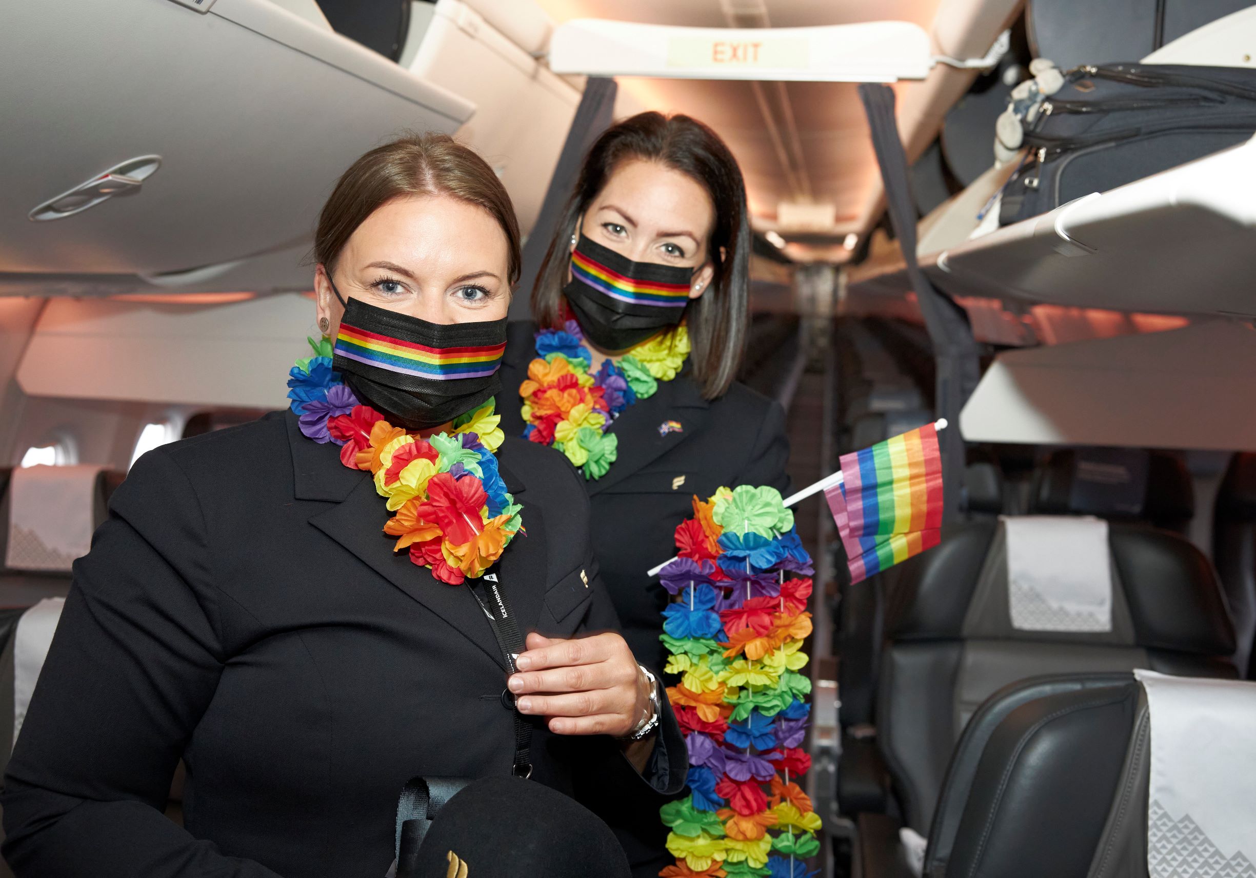 two Icelandair cabin crew staff in the aircraft holding Pride flags, wearing Pride masks and rainbow coloured garlands