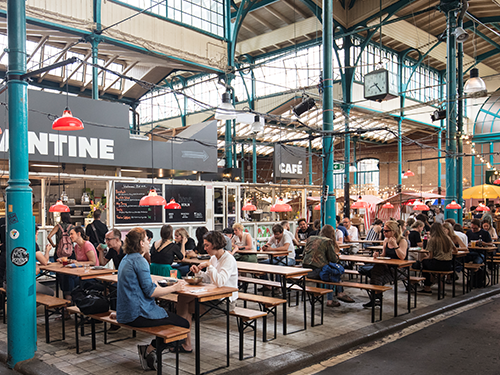 People eat with friends and family at various tables at an indoor food market in Berlin