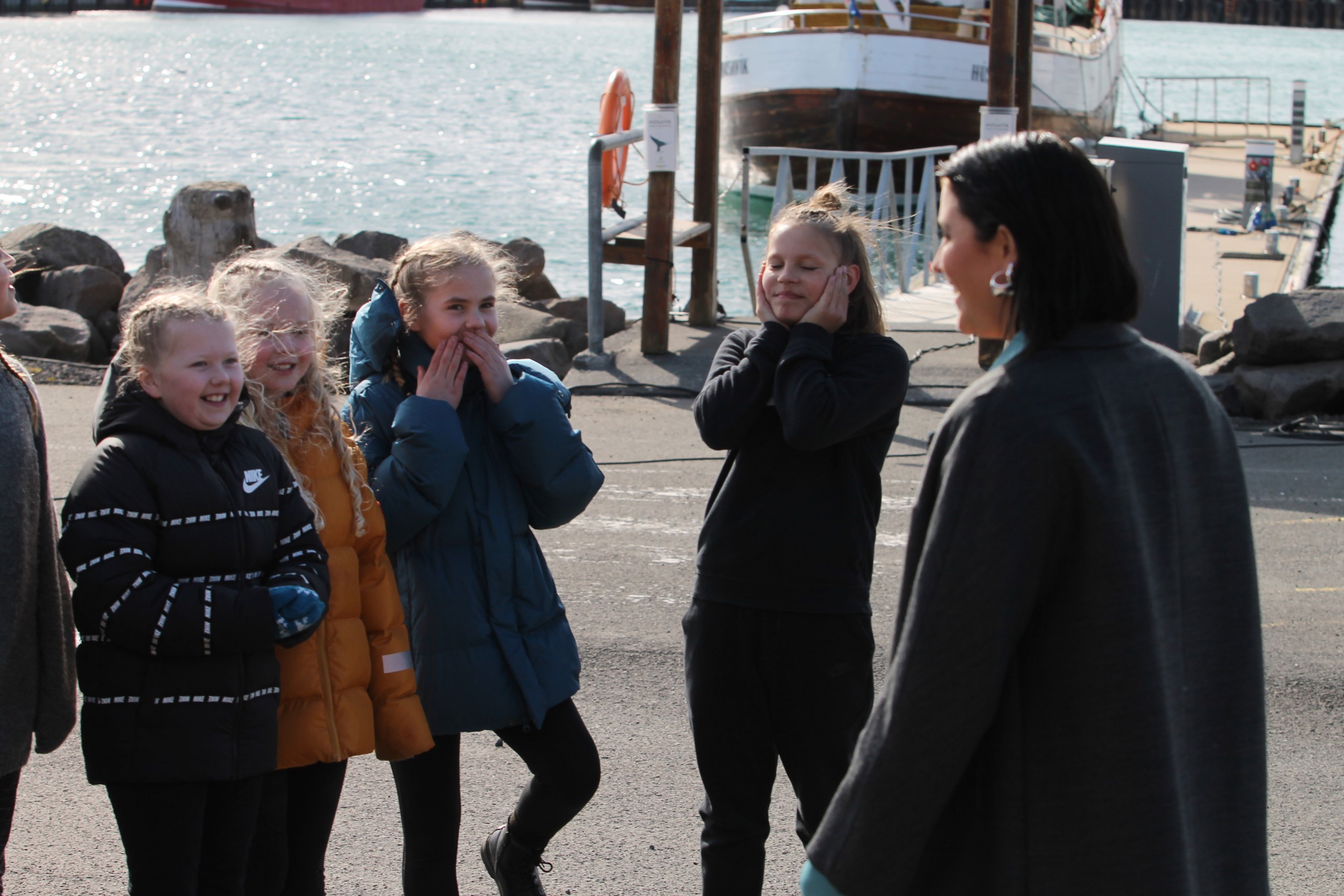 Molly Sandén standing with her back to the camera speaking to a group of young people in Husavik harbour