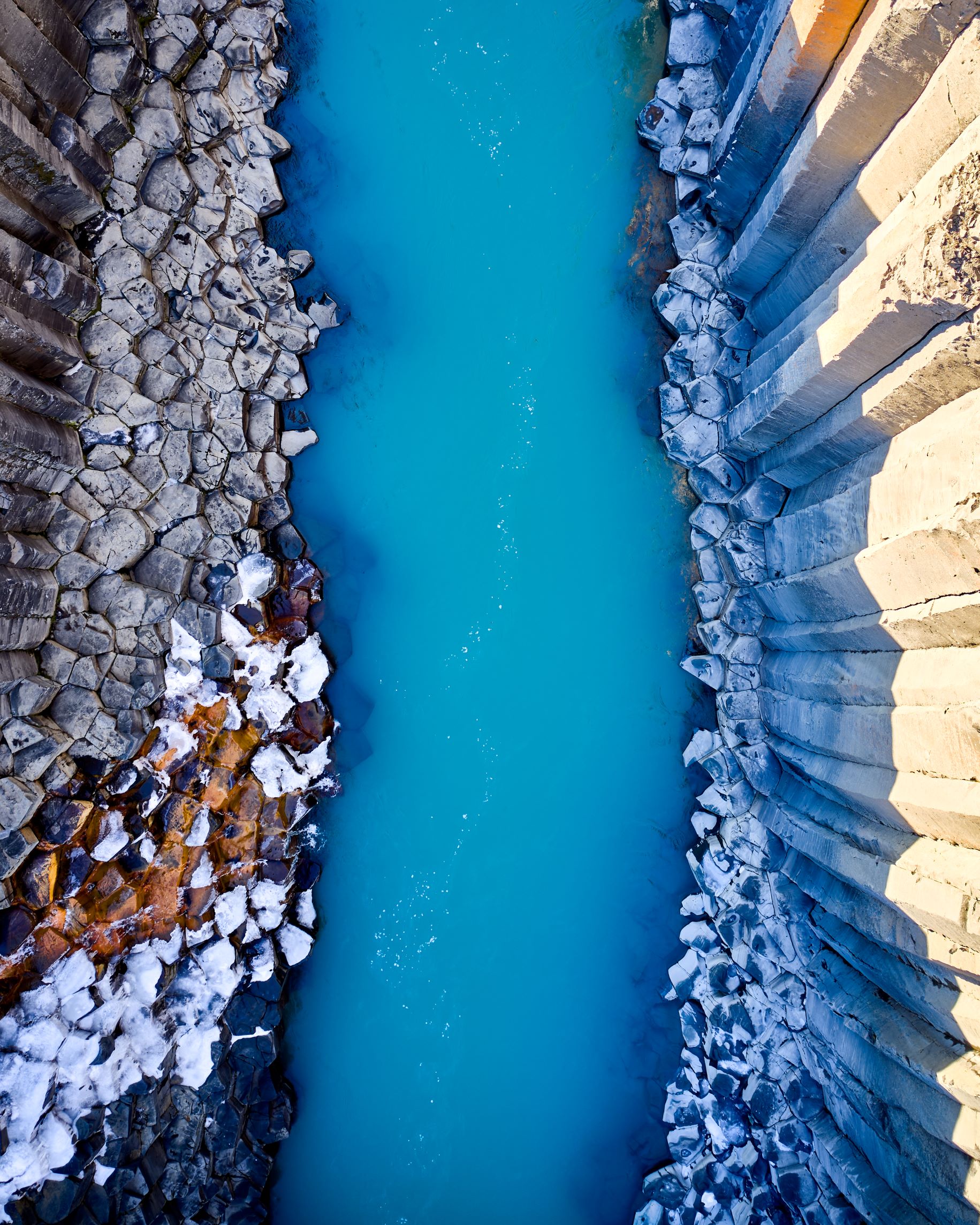 A drone shot of Stuðlagil canyon, showing the basalt columns surrounding a blue-water river