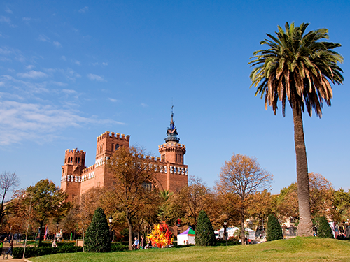 The Castle of Tres Dragons in Barcelona, pictured with a palm tree in the foreground on a bright sunny day 