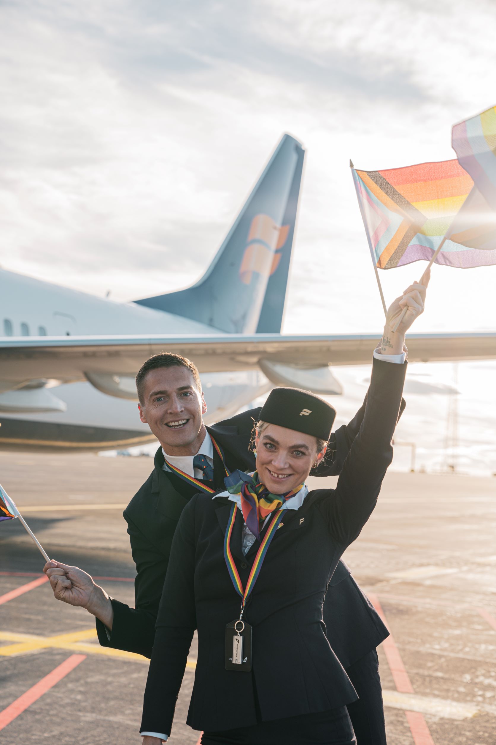 Icelandair Pride flight 2022: 2 cabin crew stand in front of aircraft waving rainbow flags