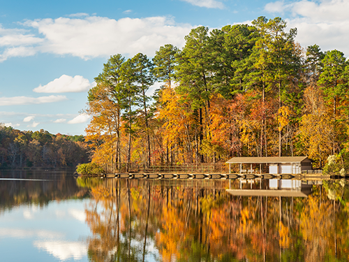 Umstead Park pictured from across a body of water, with the trees lit up in autumnal colours 