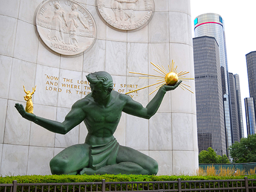 The Spirit of Detroit statue pictured on an overcast day, with high rise buildings in the background 