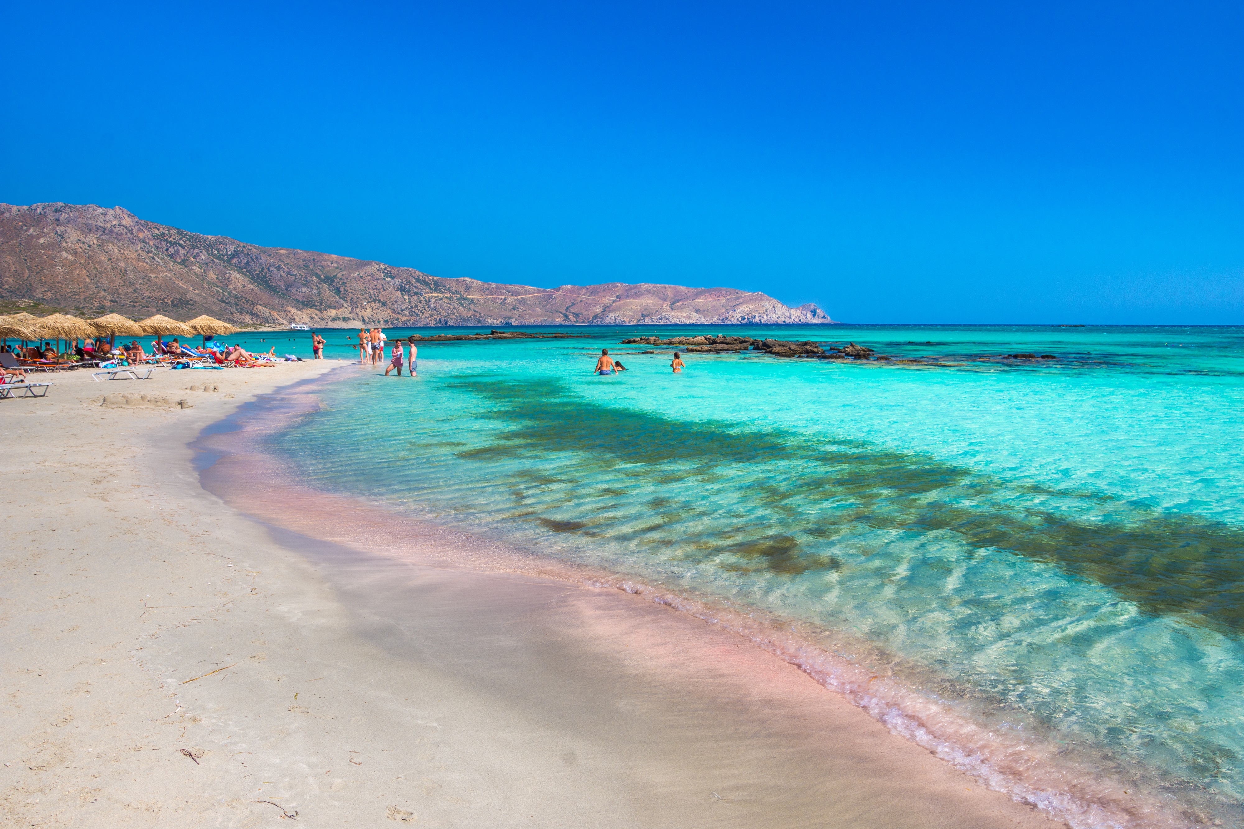 People in the distance enjoy a beautiful white sand beach in Crete, with crystal blue sea water 