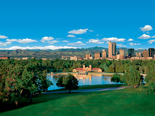 A stunning scene of City Park in Denver, with lush greenery in the fore of the picture and red brick buildings in the background 