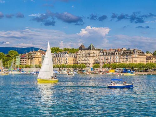 A couple of boats sail on the water with the city of Geneva in the background 