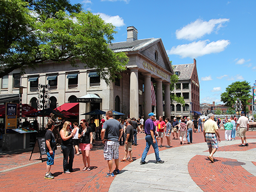Quincy Market in Boston pictured on a sunny day with groups of people enjoying the sun outdoors