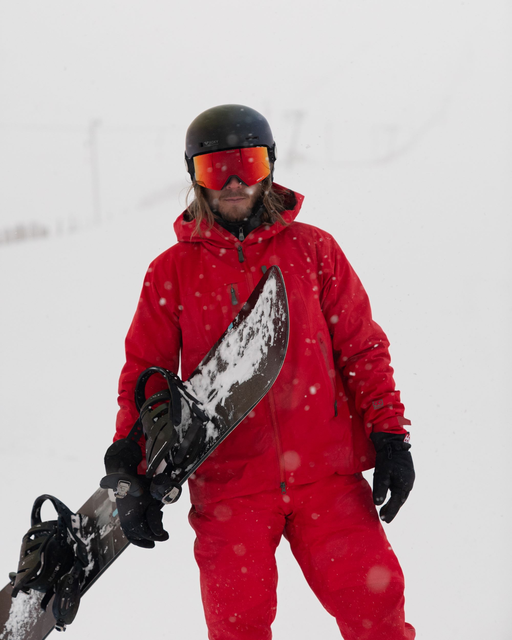Rúrik Gíslason is dressed in a red skiing outfit, wearing helmet and ski goggles and carrying a snowboard.
