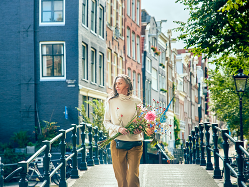 A woman holds flowers, walking across one of the canal bridges in Amsterdam, Netherlands