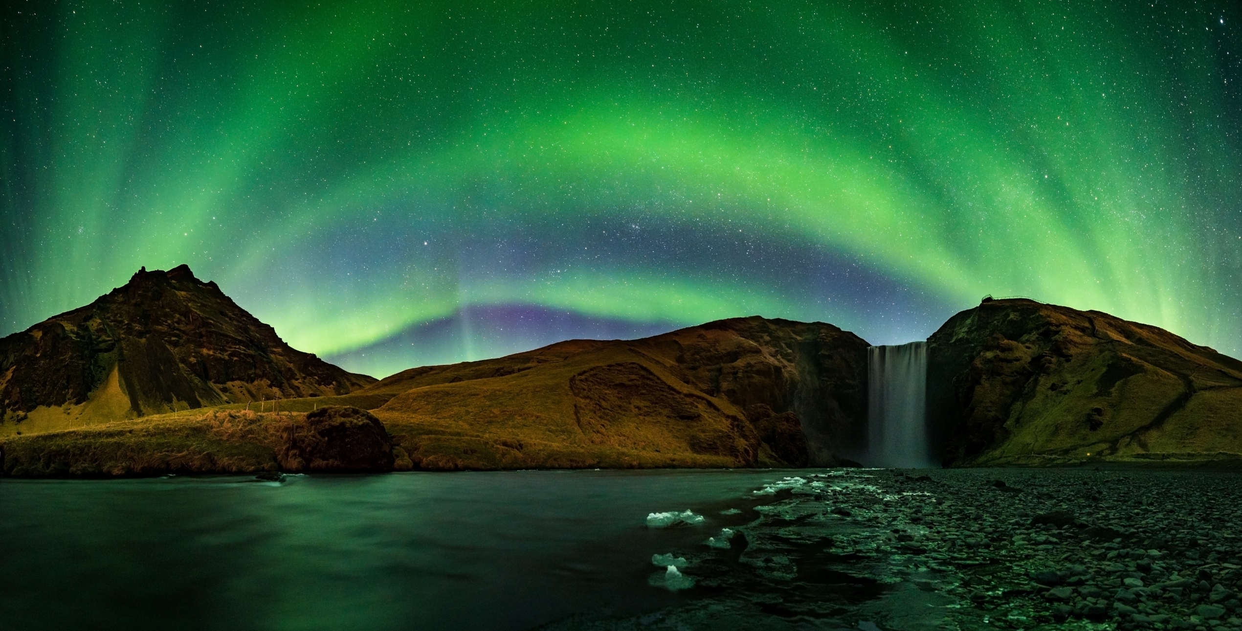 Northern lights brighten the sky above Skogafoss waterfall in South Iceland
