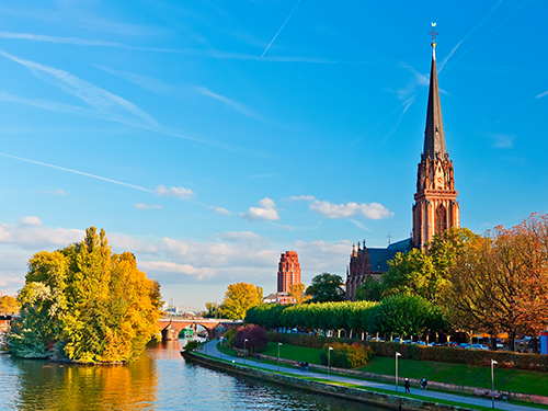 A scene of Frankfurt on a bright sunny day, with the greenery of the city and Dreikönigskirche church in view 