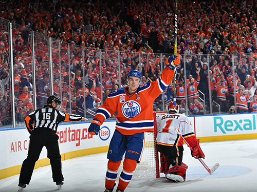 An ice hockey player celebrates after scoring, with one arm holding their stick in the air 