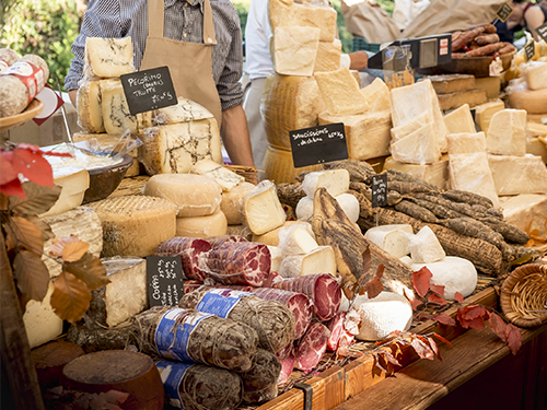 A market seller stands behind a stall filled with delicious looking meats and cheeses in Nice, France 