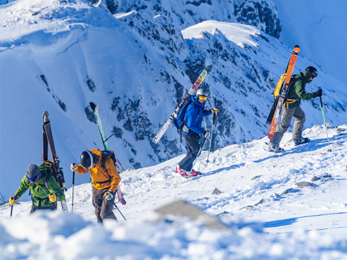 A group of four skiers hike up the mountains in Innsbruck with skis on their back.