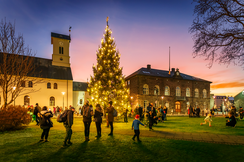 Downtown Reykjavik, in Austurvollur park square, lit up with festive cheer and families gathering around a large lit up Christmas tree