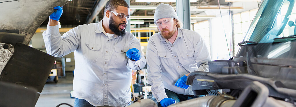 Two diesel technicians looking at the engine of a semi truck inside a maintenance shop