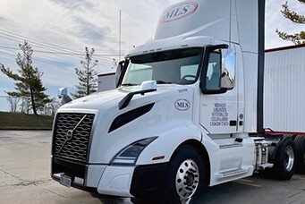 An MLS tractor parked next to a company facility