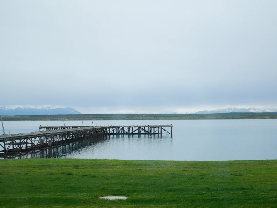 Cais de madeira em lago calmo na Patagônia chilena, com gramado em primeiro plano e montanhas distantes. Planeje com pontos Livelo.
